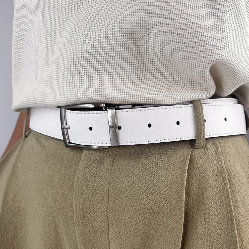 White black reversible vegan belt with a silver buckle worn by a person in beige pants and a light gray shirt.